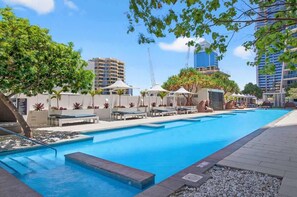 A swimming pool with lounge chairs and umbrellas, surrounded by buildings and greenery. - H Residence L19 Ocean view 2BR (Surfers Paradise)