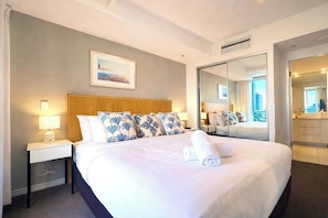 A hotel room with a large bed, a nightstand with a lamp, a mirror, and a city view. - H Residence L19 Ocean view 2BR (Surfers Paradise)