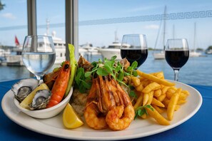 A seafood platter with shrimp, oysters, and fries, accompanied by water and wine glasses, set against a marina backdrop. - Waterview Hope Island House (Hope Island)