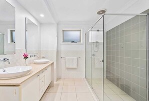 A modern bathroom with two sinks, a glass shower enclosure, and a small window. - Waterview Hope Island House (Hope Island)