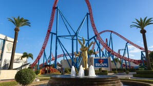 Eine Achterbahn mit blau-roter Strecke, eine goldene Statue im Vordergrund und ein Schild mit der Aufschrift 'ESCAPE'.