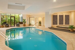 An indoor swimming pool with a sunlit room, a seating area with chairs, and a spa area with a hot tub. - Ocean View 2BR apartment with Spa (Surfers Paradise)