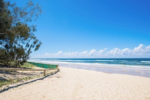 A beach with a wooden fence, a clear blue sky, and ocean waves. - Ocean View 2BR apartment with Spa (Surfers Paradise)