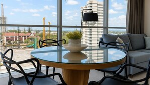A modern room with a glass table, chairs, a sofa, and a view of a cityscape. - Surfers 1BR Retreat: Pool, Spa, Gym & Fast Wi-Fi (Surfers Paradise)