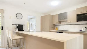 A modern kitchen with a central island, bar stools, a clock, and a microwave. - Dreamworld Home with Pool, BBQ, WI-FI and Backyard (Oxenford)