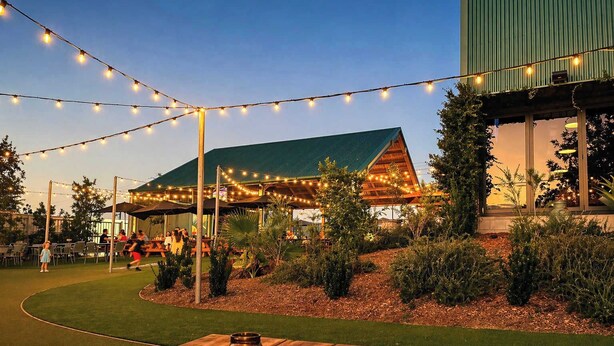 An outdoor dining area with string lights, a wooden table, and a building with a green roof. - Dreamworld Home with Pool, BBQ, WI-FI and Backyard (Oxenford)