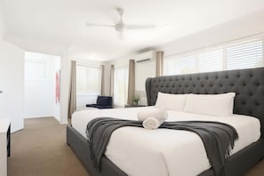 A bedroom with a large bed, a ceiling fan, and a window with blinds. - Dreamworld Home with Pool, BBQ, WI-FI and Backyard (Oxenford)