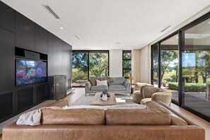 A modern living room with a large flat-screen TV, a grey sofa, a brown leather couch, and a coffee table.