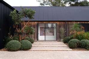 Un bâtiment moderne à l’extérieur sombre, doté d’une porte d’entrée en verre et d’un chemin en béton menant à la porte.