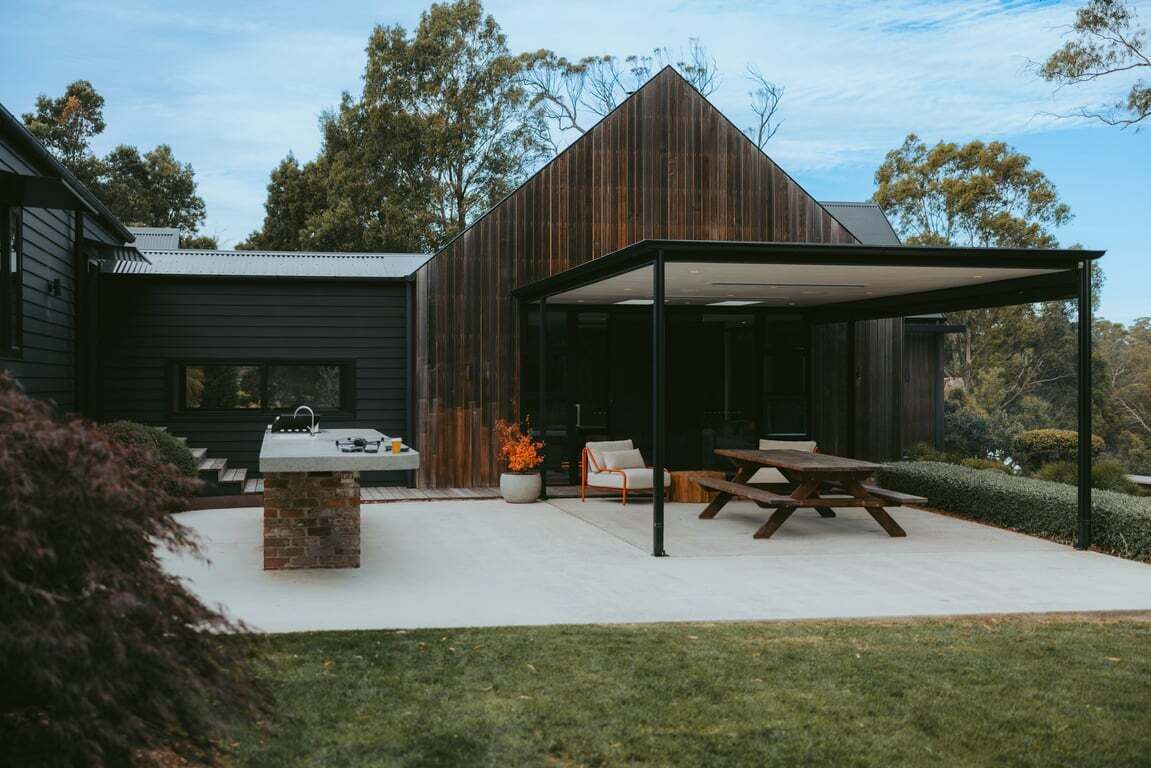 Una casa moderna con un'area esterna coperta, un barbecue e un angolo salotto.