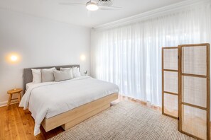 A bedroom with a bed, a nightstand, a ceiling fan, and sheer curtains. - Casaba Villa - Your Beachside Garden Oasis (Glenelg South)