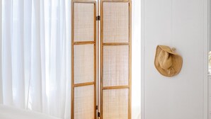 A bedroom with a bed, white curtains, a woven screen door, and a straw hat on the wall. - Casaba Villa - Your Beachside Garden Oasis (Glenelg South)