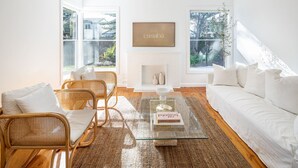 A modern living room with a fireplace, wicker furniture, and a bookshelf. - Casaba Villa - Your Beachside Garden Oasis (Glenelg South)