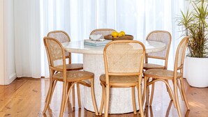 A dining area with a round table, four wicker chairs, a potted plant, and a white curtain. - Casaba Villa - Your Beachside Garden Oasis (Glenelg South)