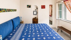 Un dormitorio con una cama, un banco de madera, una ventana con cortinas y un ventilador de techo.