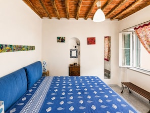 Ein Schlafzimmer mit einem Bett, einer hölzernen Bank, einem Fenster mit Vorhängen und einem Deckenventilator.