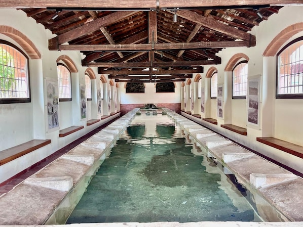 Ein langer Korridor mit einem zentralen Pool, Bogenfenstern und einer Holzbalkendecke.