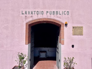 Ein Eingang zum LAVATOIO PUBBLICO mit einem Ziegelbogen und einem Schild an der Wand.