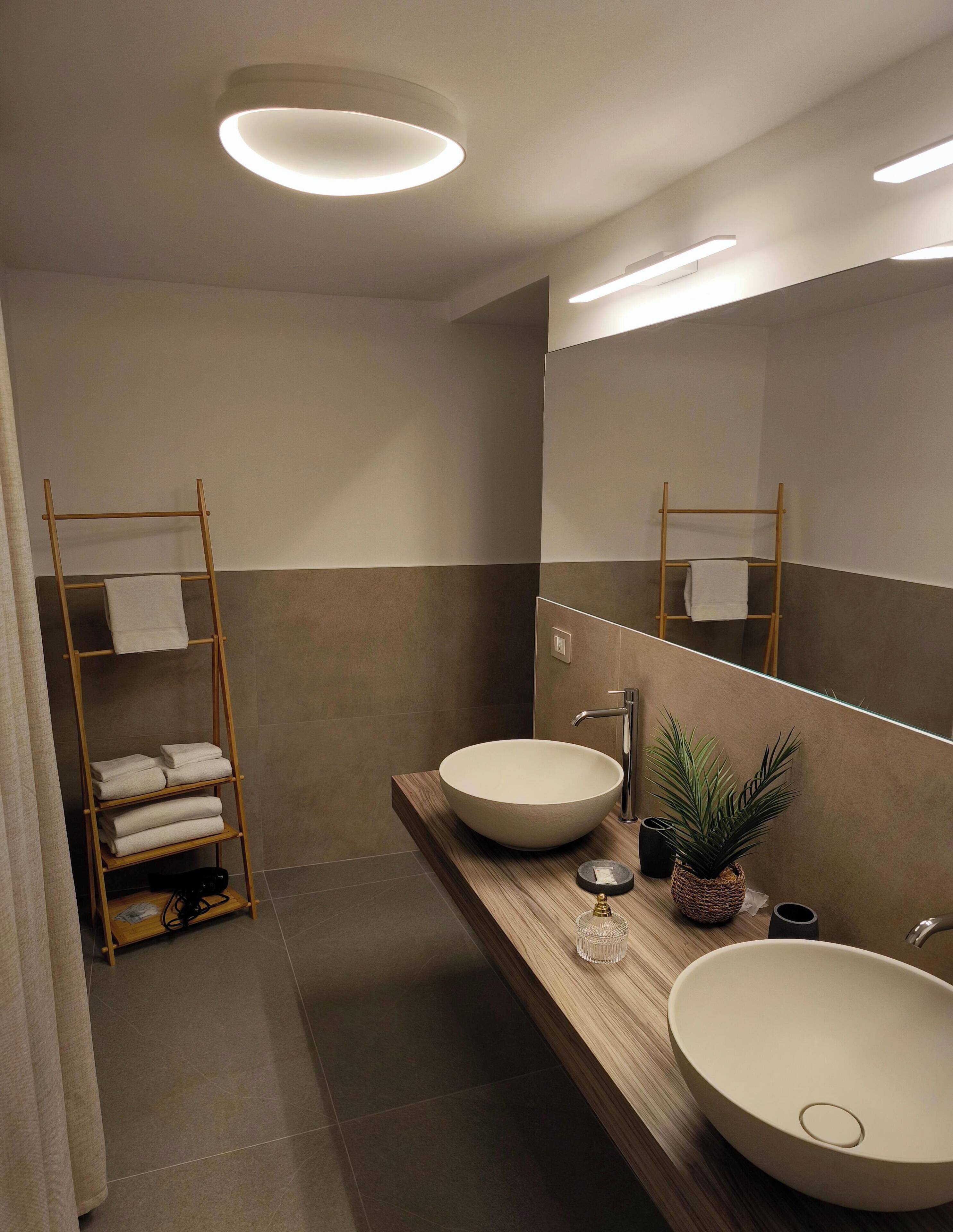 Een moderne badkamer met twee grote wasbakken, een houten handdoekhouder, een spiegel en inbouwspots.