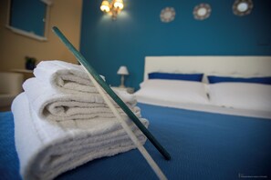 A neatly folded stack of white towels with a green-handled brush on a blue bedspread in a room with a blue wall and a white headboard. - Luxury B&B Villa Bellini: A Haven Just 5 Minutes from Downtown (Catania)