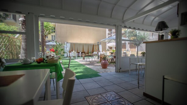 A covered outdoor dining area with tables and chairs, a green lawn, and a view of the street. - Luxury b&b Villa Bellini: residential oasis 5 minutes from downtown (Catania)