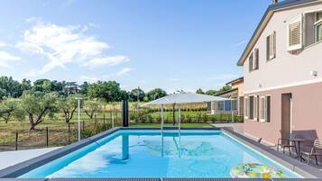 Ein Swimmingpool mit Pergola, Sitzgelegenheiten im Freien und Blick auf die umliegende Landschaft.