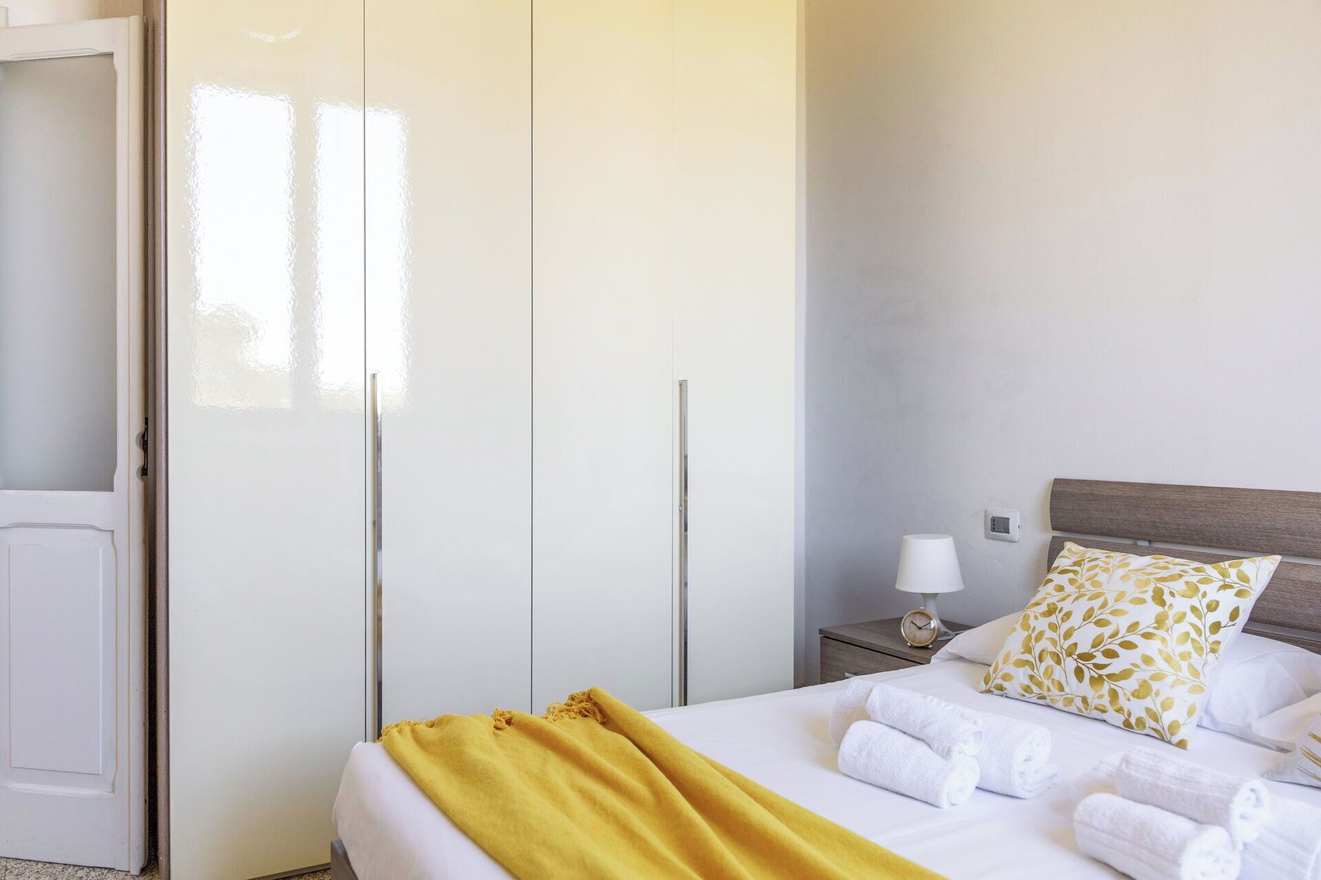 Una camera d'albergo con un letto, un comodino con una lampada, una scrivania e un armadio.