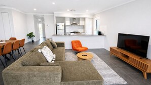 En moderne stue med sofa, sofabord, orange lænestol, fjernsyn og et køkken i baggrunden.