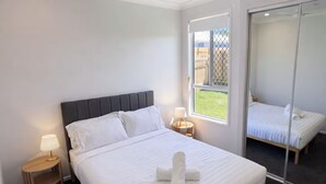 Et moderne soveværelse med en stor seng, en loftsvift, sengeborde med lamper og en skydedør, der fører ud til en balkon.