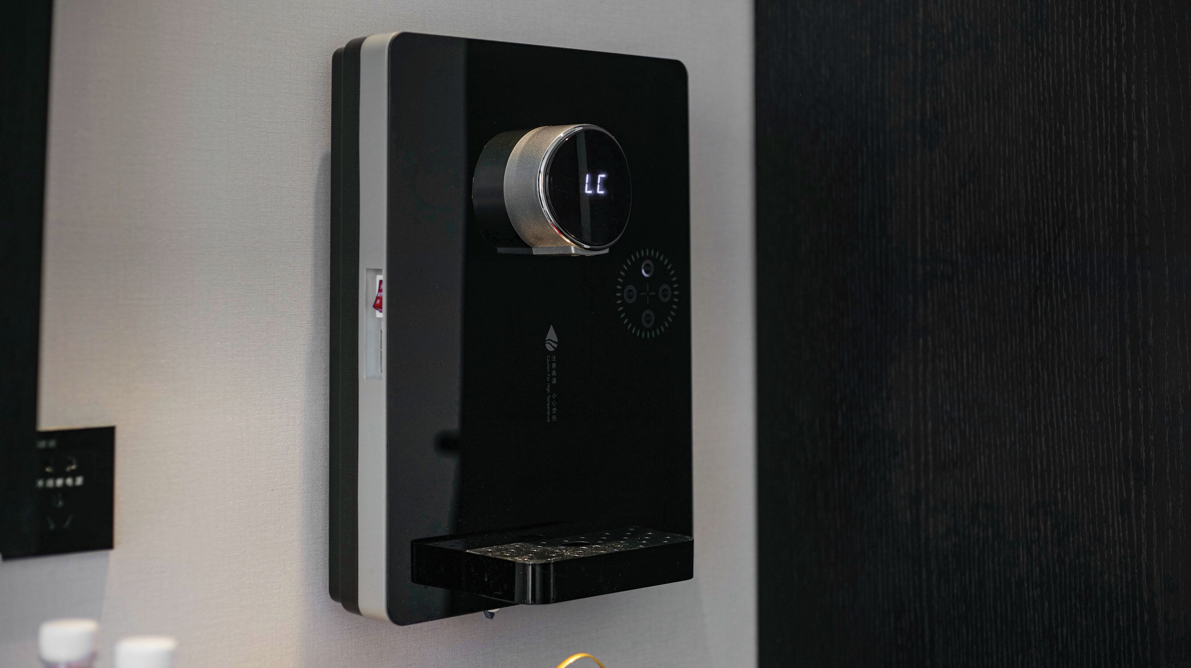 A black wall-mounted device with a circular dial and a small display.