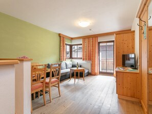 A cozy living room with a sofa, a dining table with chairs, a television, and a window with curtains. - Beautiful apartment near the ski bus to Sölden (Huben)