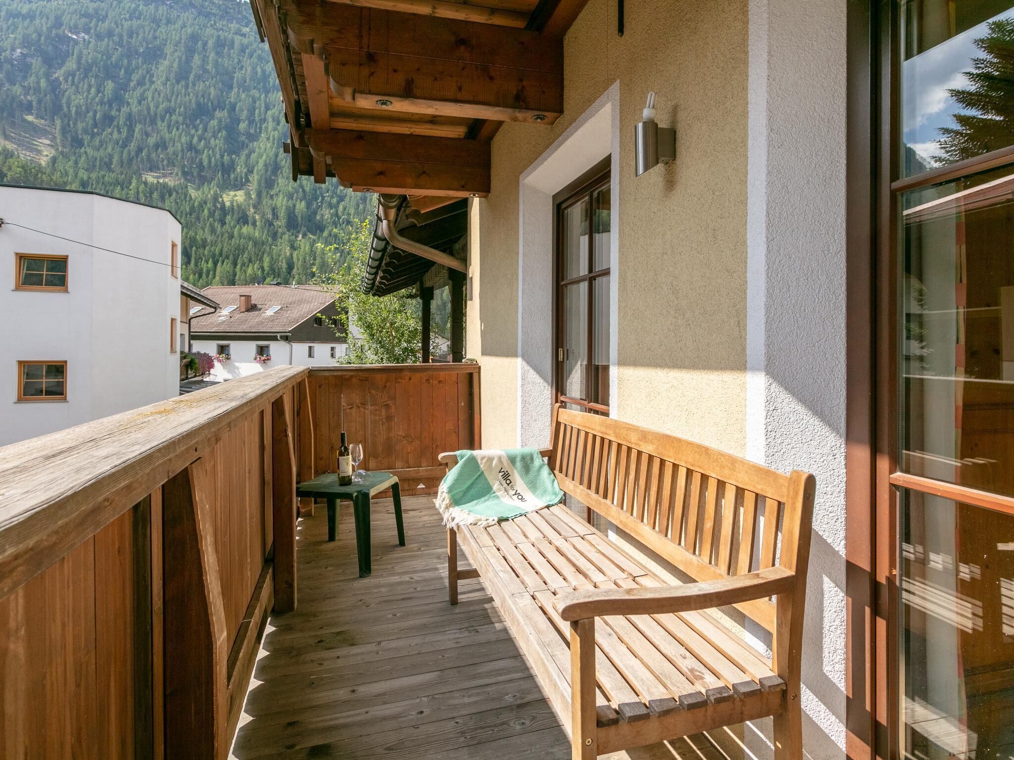 Un balcon en bois, agrémenté d’un banc et d’une table, qui offre une vue sur un paysage montagneux.