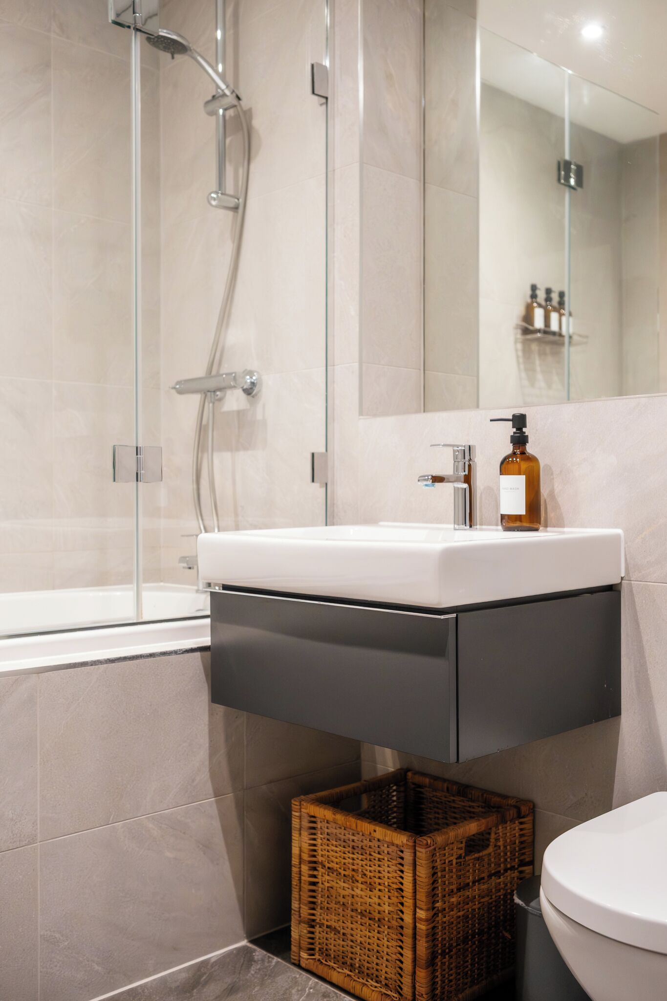Ein modernes Badezimmer mit einer Duschkabine aus Glas, einem weißen Waschbecken mit schwarzem Unterschrank und einem Korbwannen-Korb.