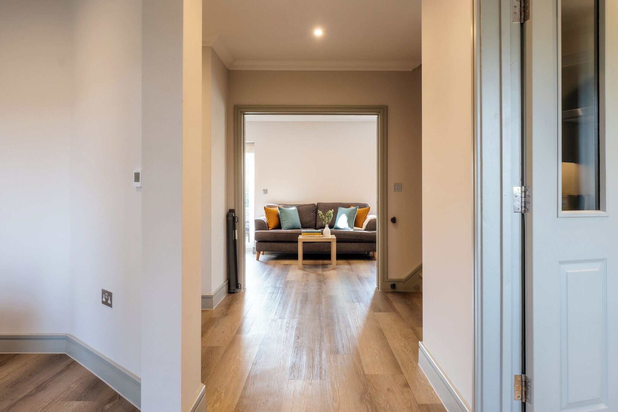 A hallway leading to a living room with a sofa, a coffee table, and a door.