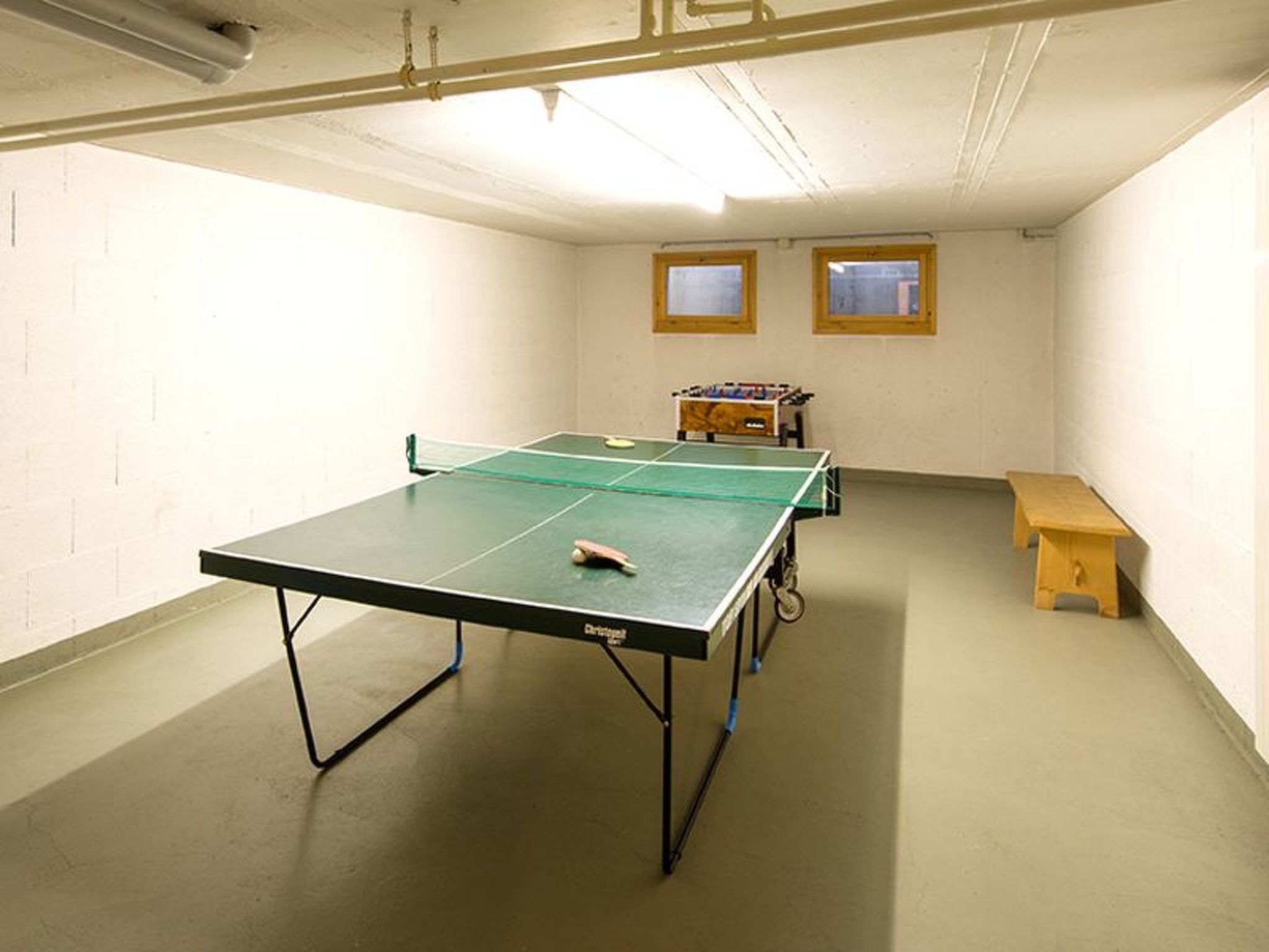 Una mesa de ping pong en una habitación con un banco y una mesa de futbolín.