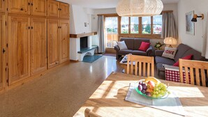 A spacious living area with wooden cabinets, a sofa, a dining table with fruit, and a large window.