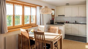 A modern kitchen with white cabinets, a dining table with wooden chairs, and a large window with curtains.