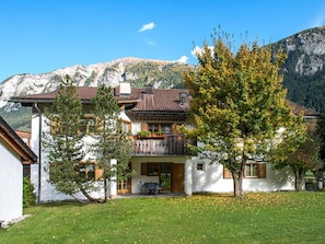 Ein zweistöckiges Gebäude mit Balkon, umgeben von einer Grünfläche und einem Bergpanorama.