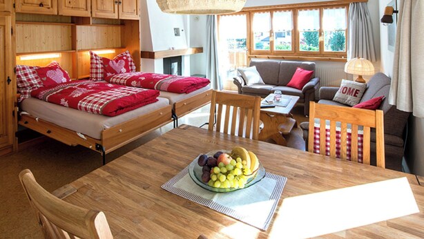 A cozy room with a bed, a sofa, a dining table with fruit, and a window with curtains.