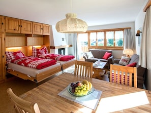 Ein gemütliches Zimmer mit einem Bett, einem Esstisch mit Obst, einer Couch und einem Fenster mit Vorhängen.