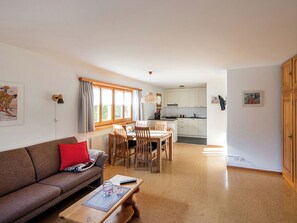 A living room with a sofa, a dining table with chairs, a kitchen area, and a window with curtains. - Ferienhaus Muntschi, (Andeer), by Interhome (Andeer)