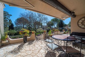 Eine Terrasse im Freien mit Steinboden, Metallmöbeln und Blumentöpfen.