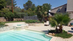 Une piscine bordée de pierres, un palmier et une chaise dans un jardin aménagé.