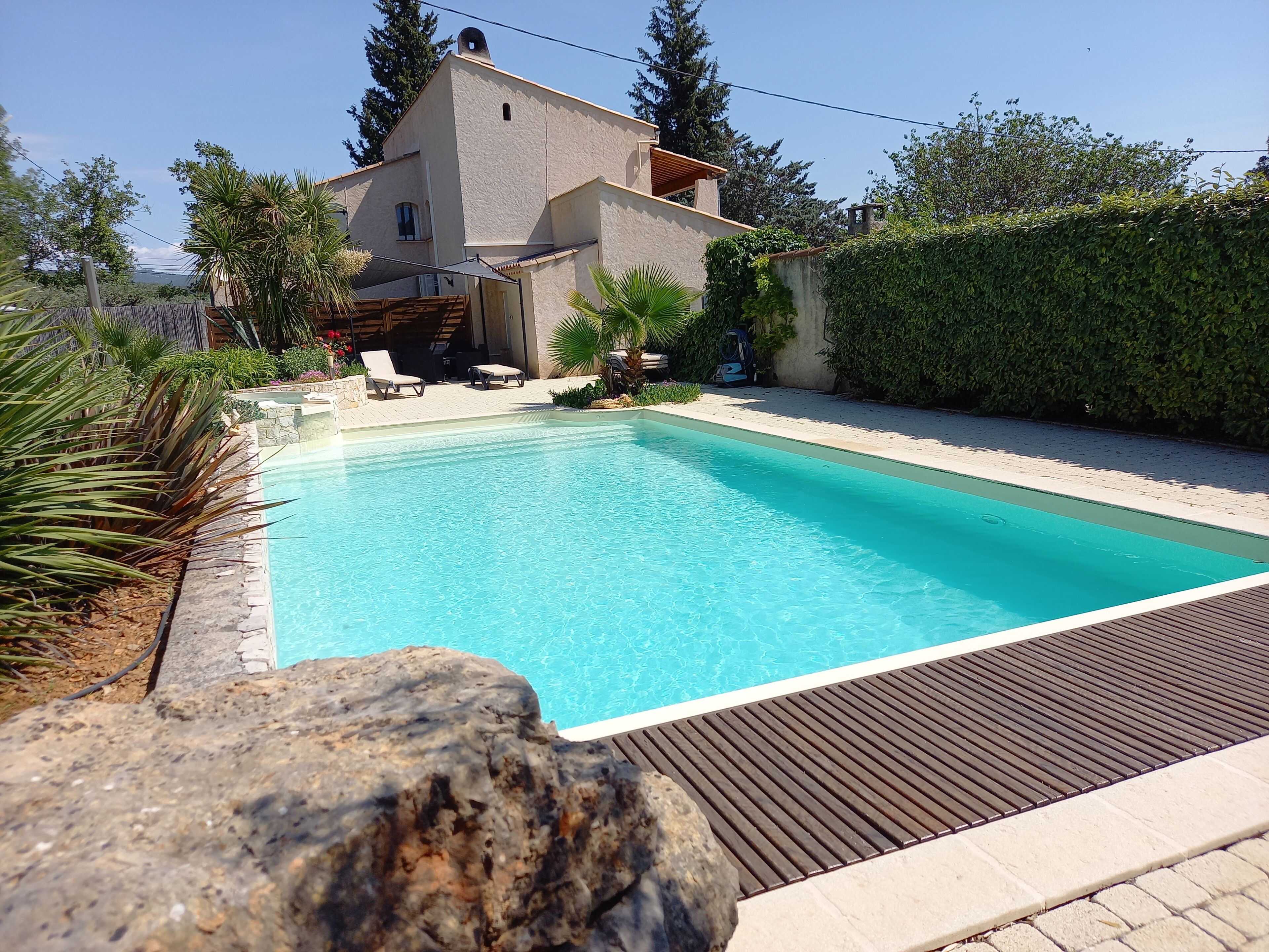 A swimming pool with lounge chairs, a stone wall, and a building with a sloped roof.