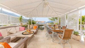 Een terras buiten met een overdekte zithoek, een eettafel en stoelen.
