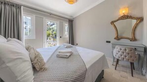 Een slaapkamer met een groot bed, een kaptafel met spiegel en uitzicht door een raam.