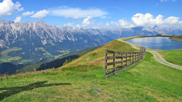 A mountain landscape with a wooden fence, a lake, and a clear sky. - Apartment  by Interhome (Saalbach-Hinterglemm)