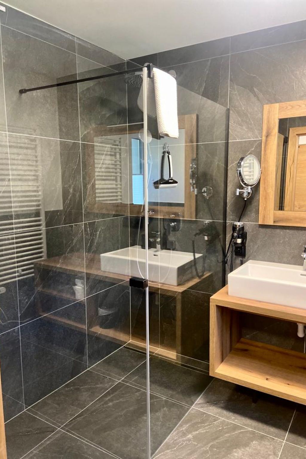 Ein modernes Badezimmer mit einer gläsernen Duschkabine, zwei Waschbecken und einem Holz-Waschtisch.