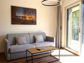 Ein Wohnzimmer mit grauem Sofa, einem Couchtisch, einem Sonnenuntergangsgemälde und einem großen Fenster.