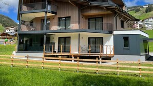 A two-story building with a balcony, large windows, and a wooden fence in the foreground. - Apartment  by Interhome (Saalbach-Hinterglemm)